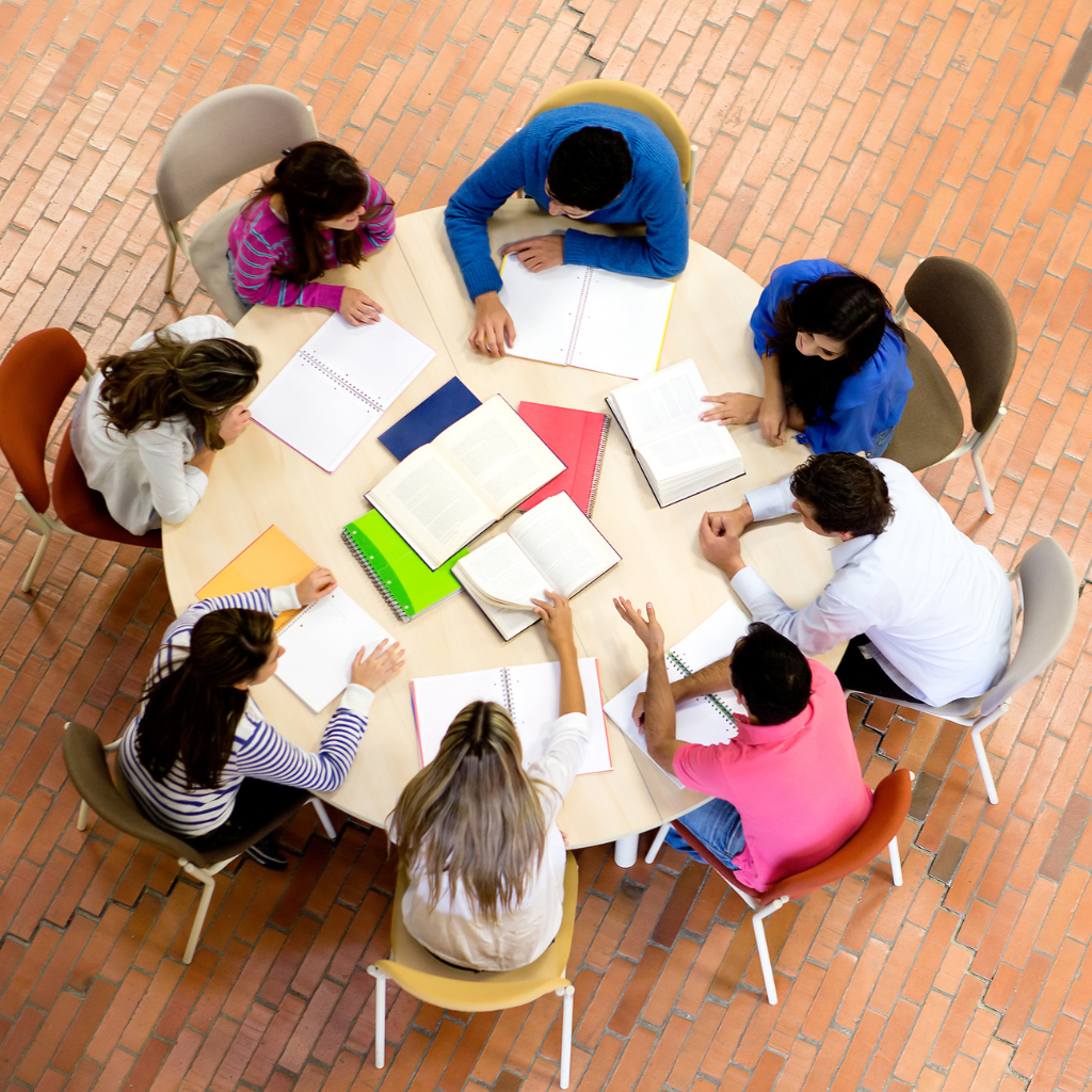 An above view of a group of people around atable, with books and papers in the middle of the table
