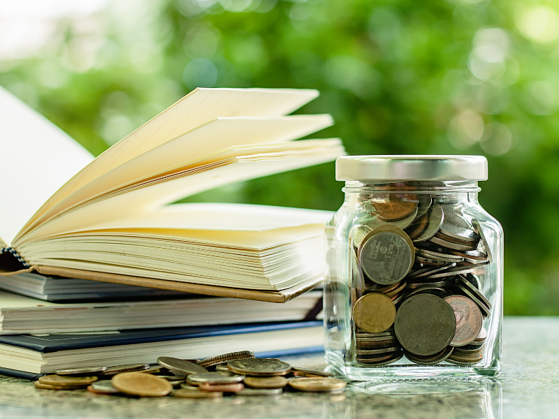 A jar of coins and coins on a table next to an open book