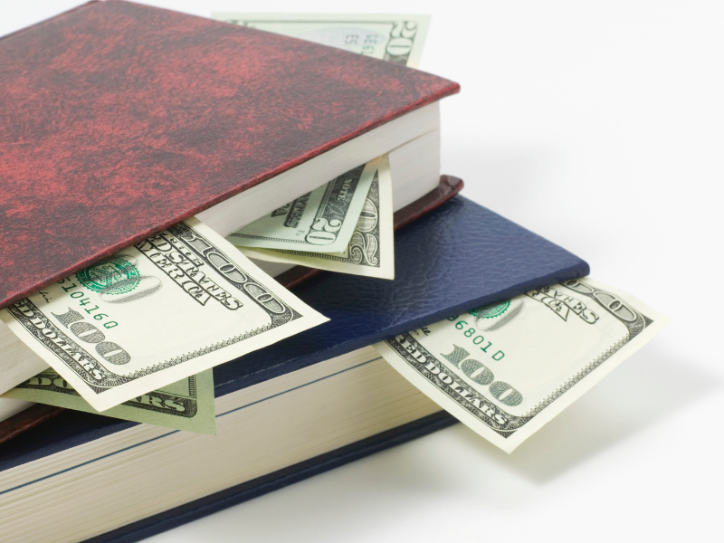 Dollar bills sticking out of a stack of books
